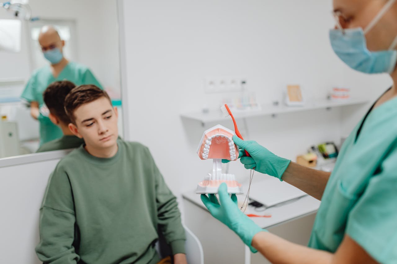 Teenager learning dental hygiene from dentist using a dental model.